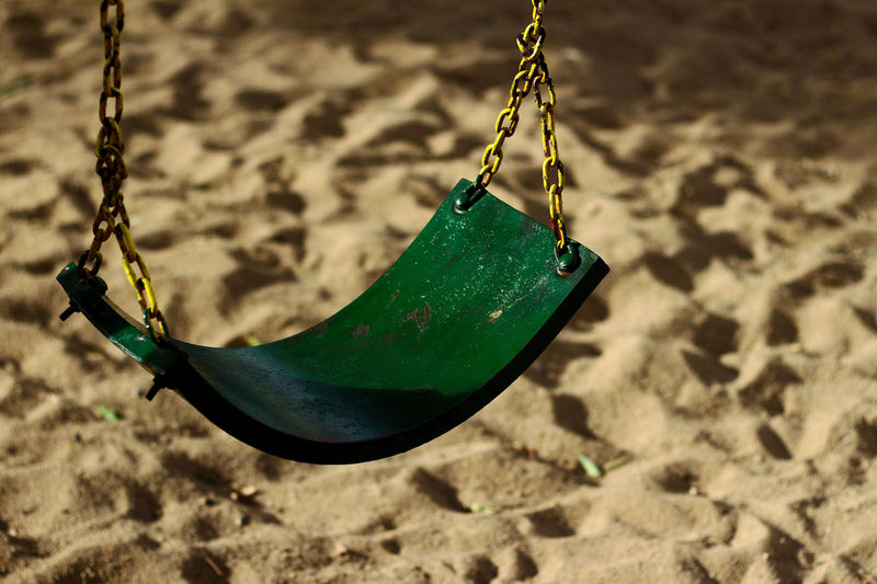High angle view of empty swing hanging over sand at playground