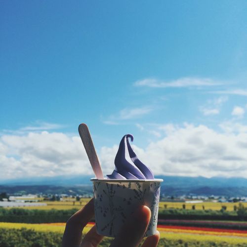 Close-up of hand holding ice cream against landscape