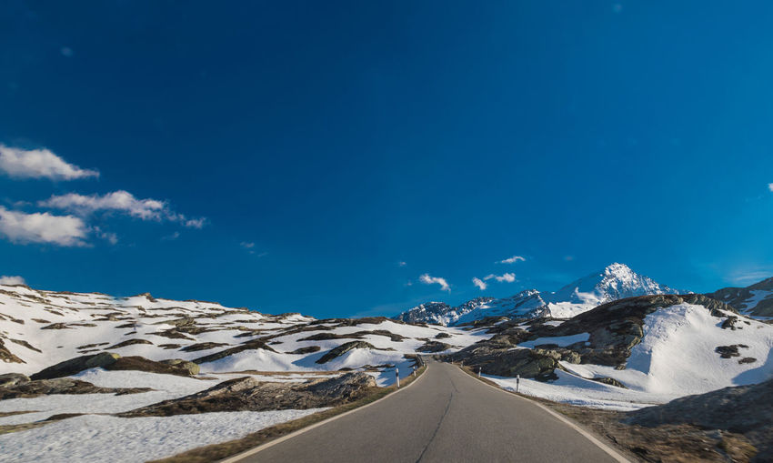 Road amidst snowcapped mountains against blue sky