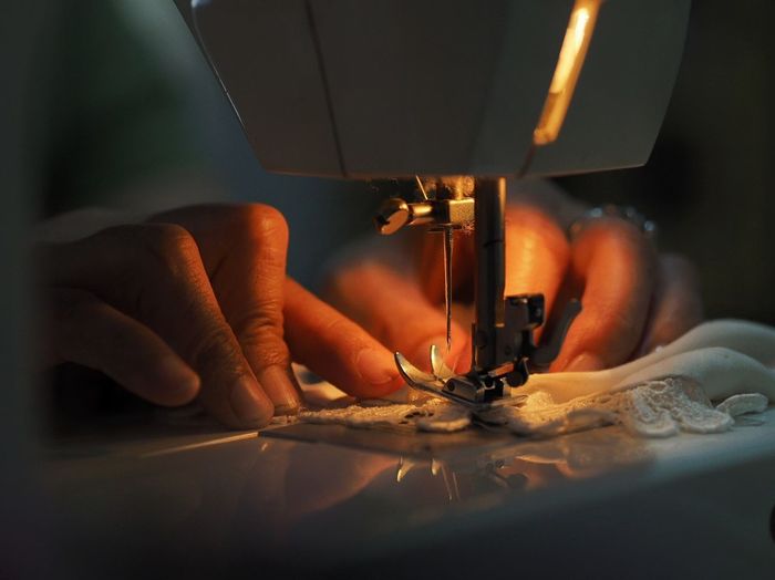 Cropped hands of woman sewing cloth in darkroom