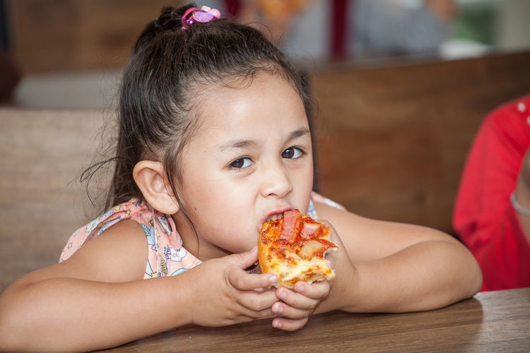 Portrait of cute girl eating pizza in classroom at school