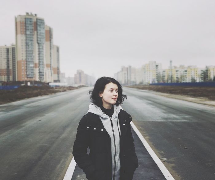 BEAUTIFUL WOMAN STANDING ON ROAD IN CITY AGAINST CLEAR SKY