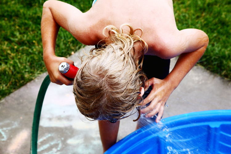 High angle view of shirtless boy holding garden hose at backyard