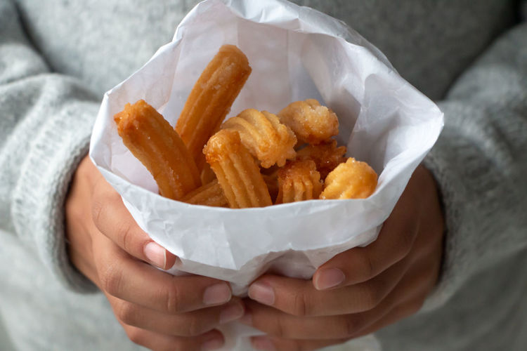 Midsection of person holding churros in paper bag