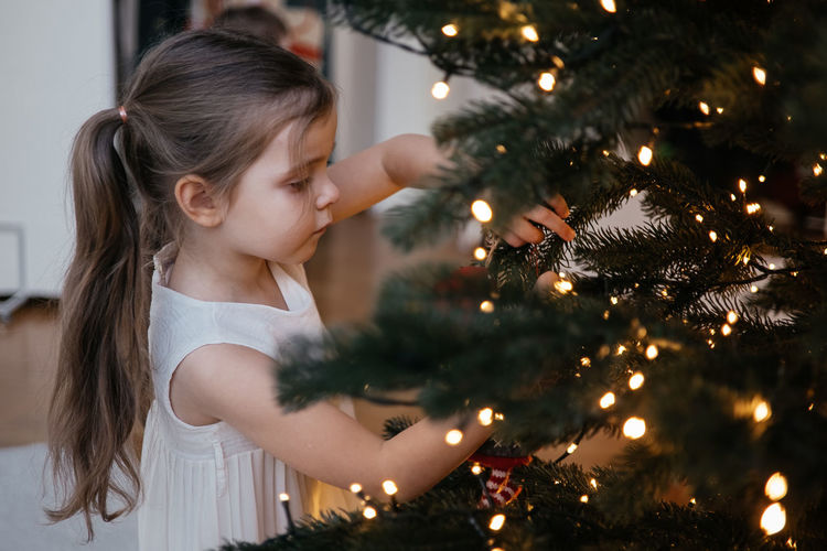 Toddler girl decorating christmas tree at home