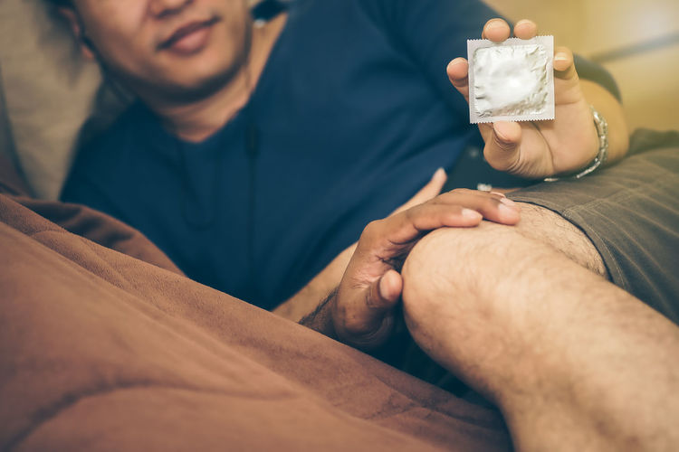 Close-up up couple holding condom lying on bed at home