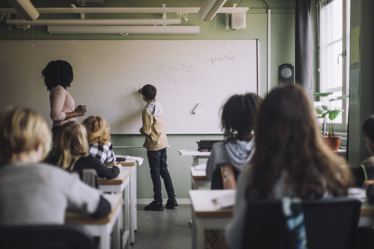 Student solving maths sum on white board in classroom