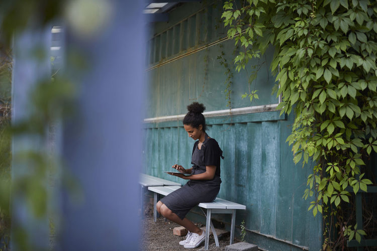 Female gardener using digital tablet while sitting on bench