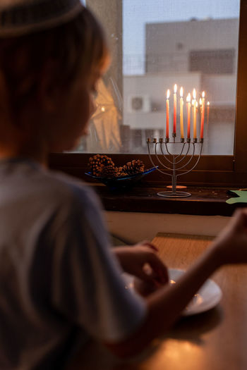 Little preschool boy lighting the hanukkah candle on a menorah. hanukkah lights. jewish boy