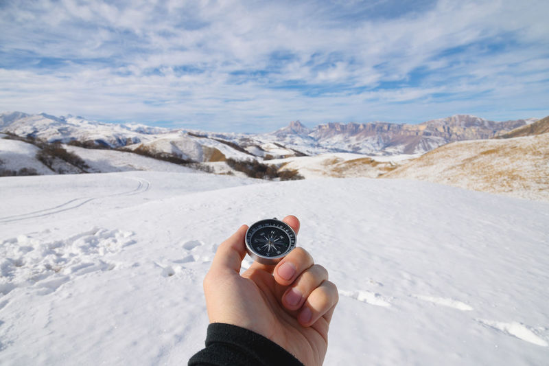 A man's hand holds a pocket magnetic compass for navigation against the backdrop of winter rocky 