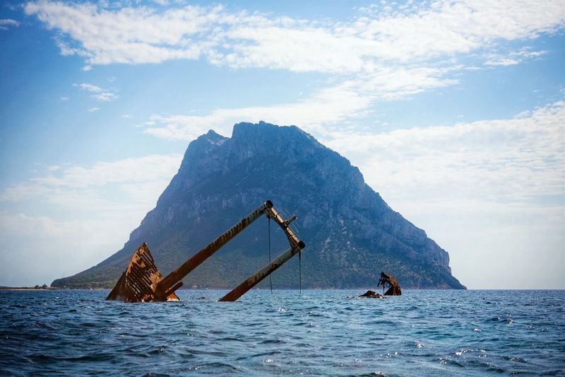Old rusty ship sinking in sea against mountain and sky