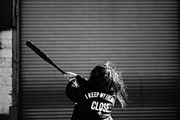 Rear view of girl playing with baseball against shutter