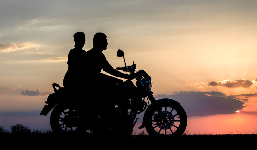 Silhouette people on motorcycle against sky during sunset