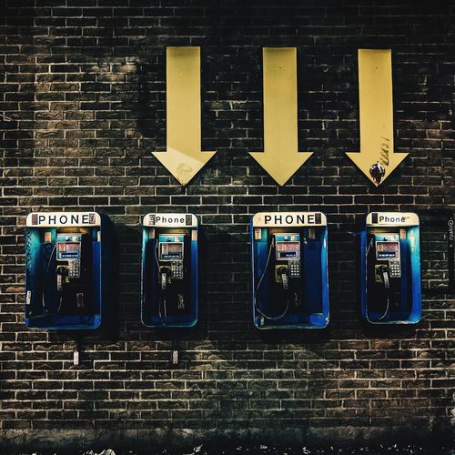 Arrow symbols directing towards pay phones on brick wall