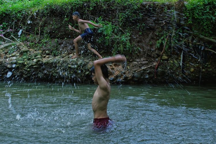 Full length of shirtless man jumping in river