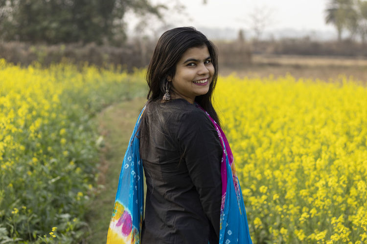 A pretty indian woman with smiling face looking back in mustard field