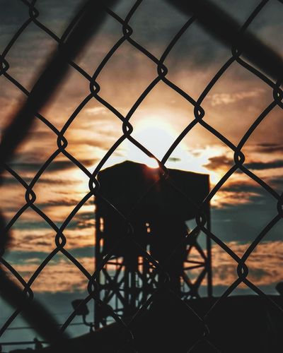 Close-up of chainlink fence against sunset sky