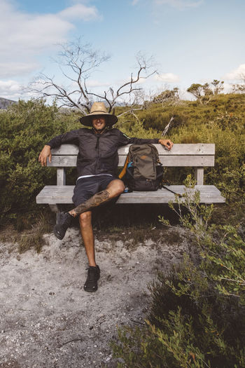 Full length of hiker with backpack wearing straw hat while sitting on bench at wilsons promontory national park
