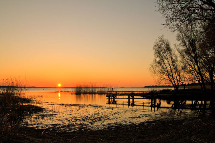 Scenic view of calm lake with pier against sky during sunset