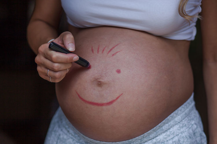 Midsection of pregnant woman making anthropomorphic smiley face on stomach