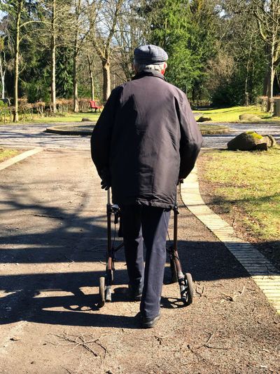Rear view of senior man with mobility walker on footpath at park during sunny day