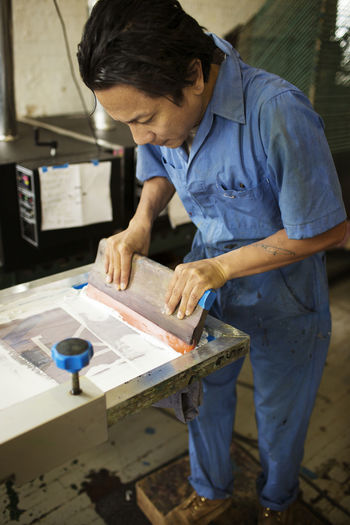 High angle view of man pressing ink on frame in workshop