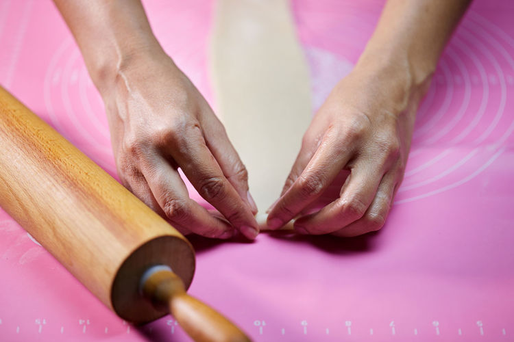 Woman's hands molding the rolle shape dough on pink silicone mesh