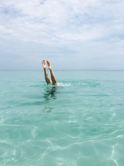 Low section of person swimming in sea against cloudy sky