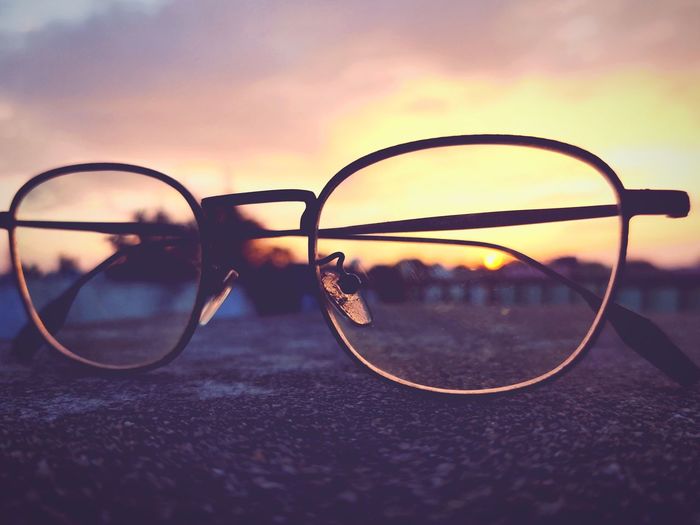 Close-up of sunglasses against sunset sky