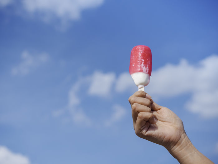 Hand holding ice cream against sky