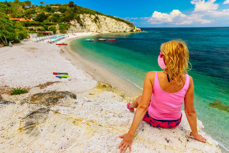 Rear view of woman wearing mask sitting on beach