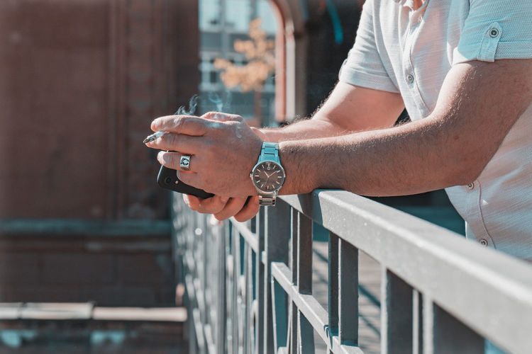 Midsection of man smoking cigarette standing on bridge outdoors