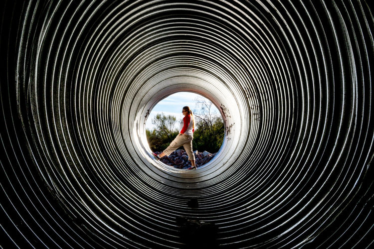 Woman standing in huge metallic pipe