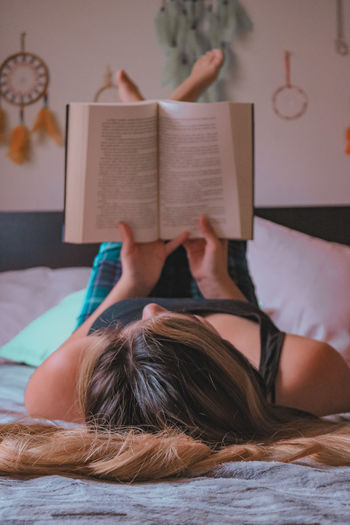 Midsection of woman reading book on bed at home