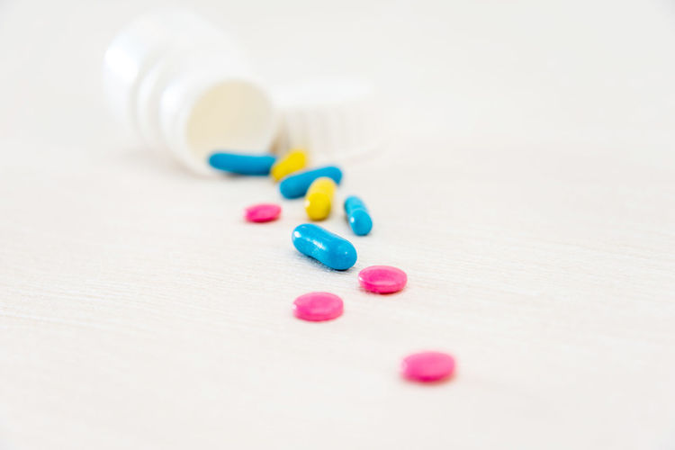 Close-up of multi colored pills with container on white background