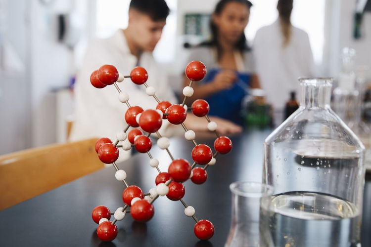Molecular structure by glassware on table against young students in chemistry laboratory