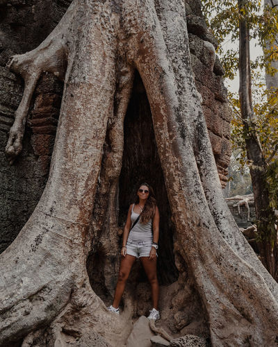 Portrait of woman standing by tree trunk