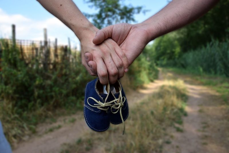 Cropped image of couple holding hands with baby booties on field