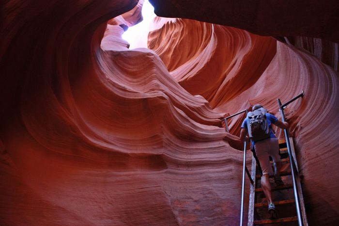 Full length rear view of tourist climbing ladder by rock formations at antelope canyon
