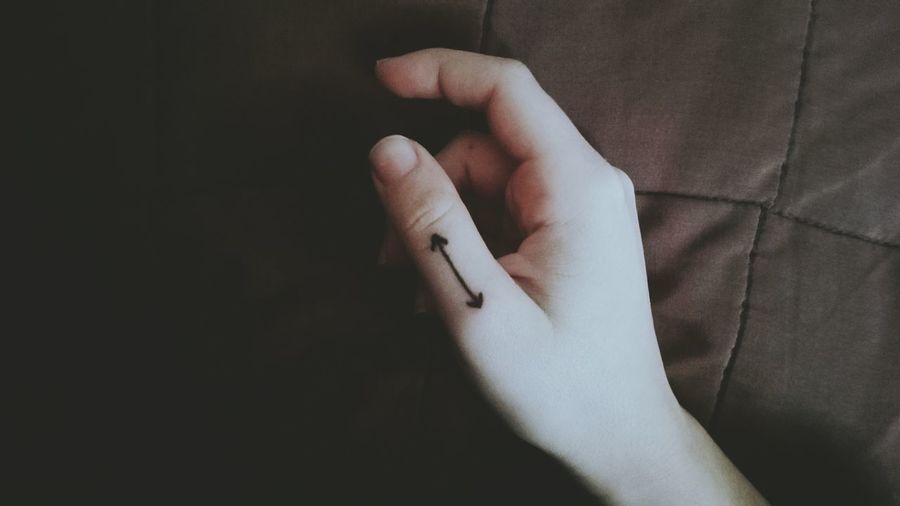 Cropped hand of woman with arrow symbol tattoo on bed