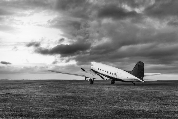 Abandoned airplane on field against cloudy sky