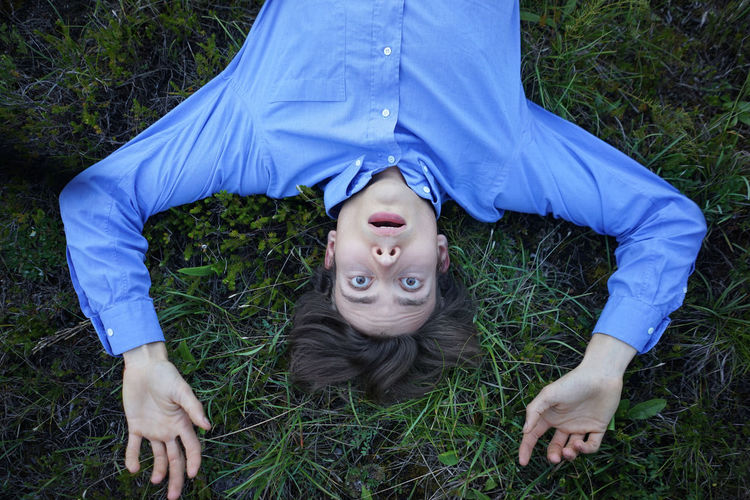 Portrait of shocked man with arms raised lying on grassy field