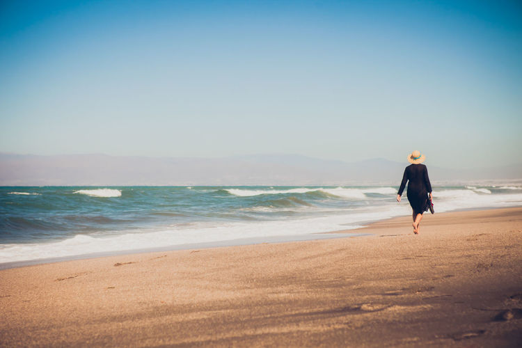 Rear view of woman walking at sea shore against clear sky