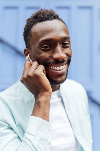 Smiling young man in casual clothing holding in-ear headphones