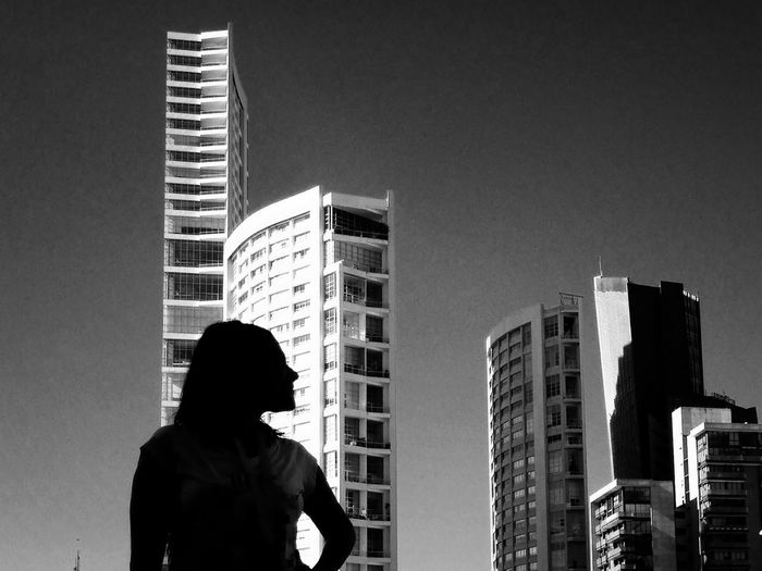 Woman standing against tall buildings against clear sky in city