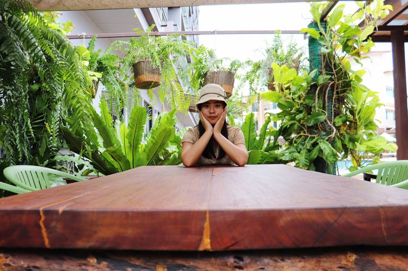 Portrait of smiling woman leaning on elbows while sitting against plants