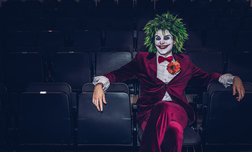 Portrait of man wearing clown costume sitting on chair