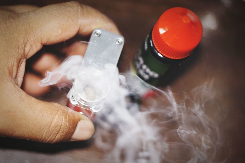 Close-up of hand holding narcotic drug with smoke emitting from bottle 