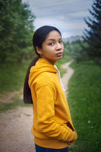 Side view of young asian girl in yellow hoodie looking at camera