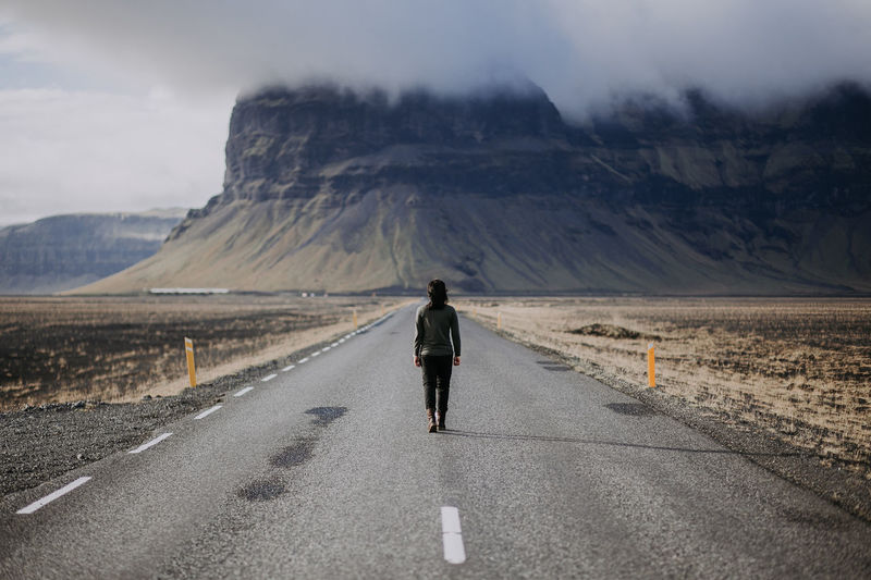 Rear view of woman walking on road against mountain